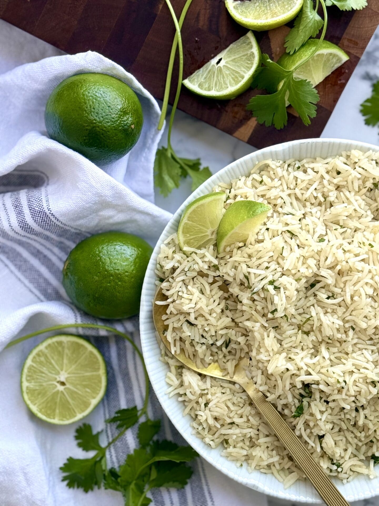 A bowl of cilantro lime rice is seen from above, surrounded by cut limes and fresh cilantro.