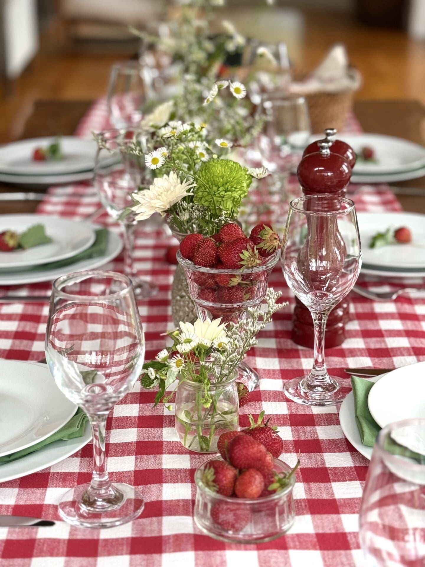 IMG_9497 A table is set with a red gingham tablecloth and vases of wild flowers for a Strawberry Social lunch. Bowls of fresh strawberries spill out onto the table.