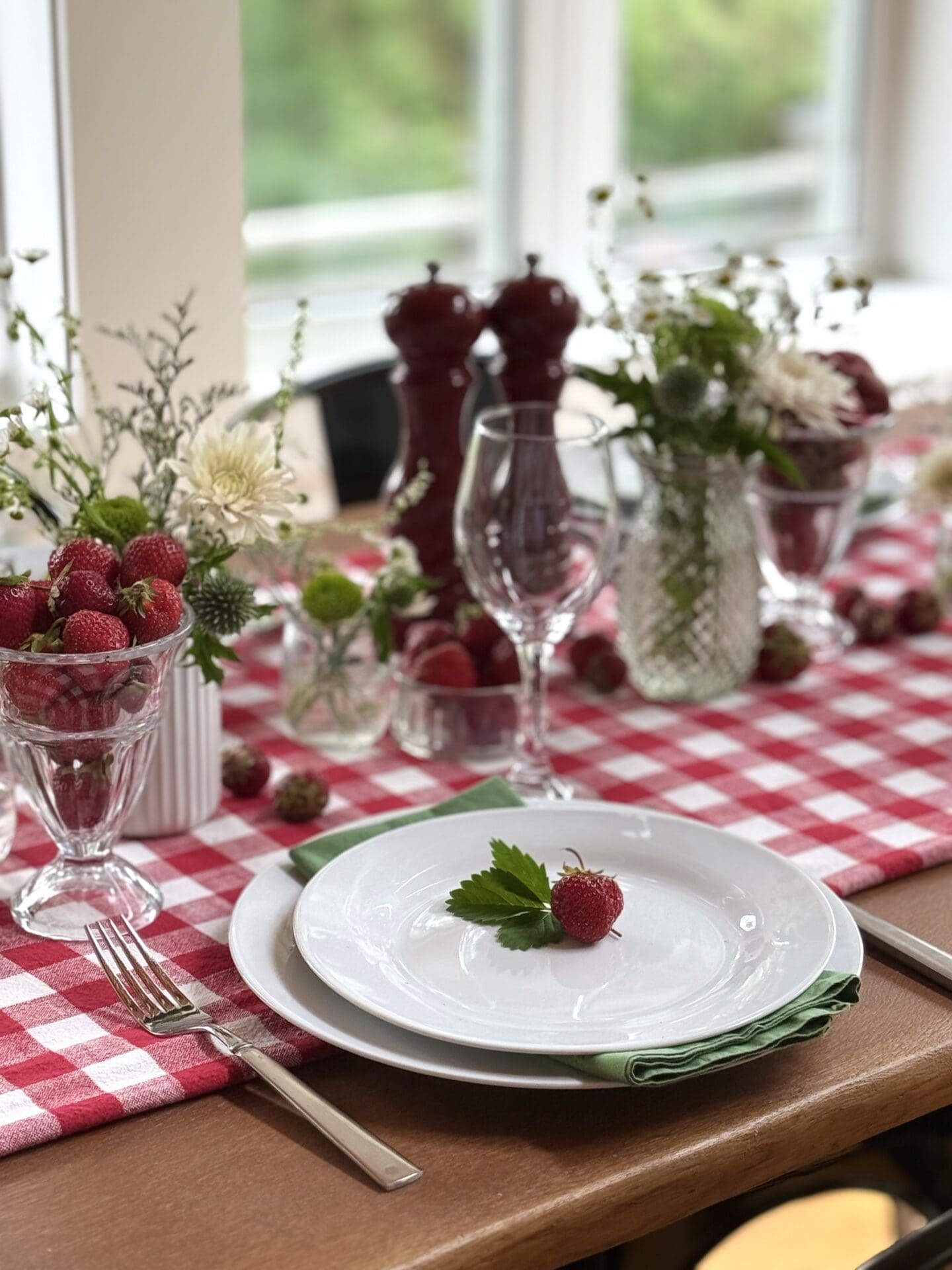 IMG_9501 The table is set in a sun-filled room for a Strawberry Social lunch. The table features a red and white gingham table cloth, mismatched vases of white and green wild flowers and plenty of fresh strawberries.