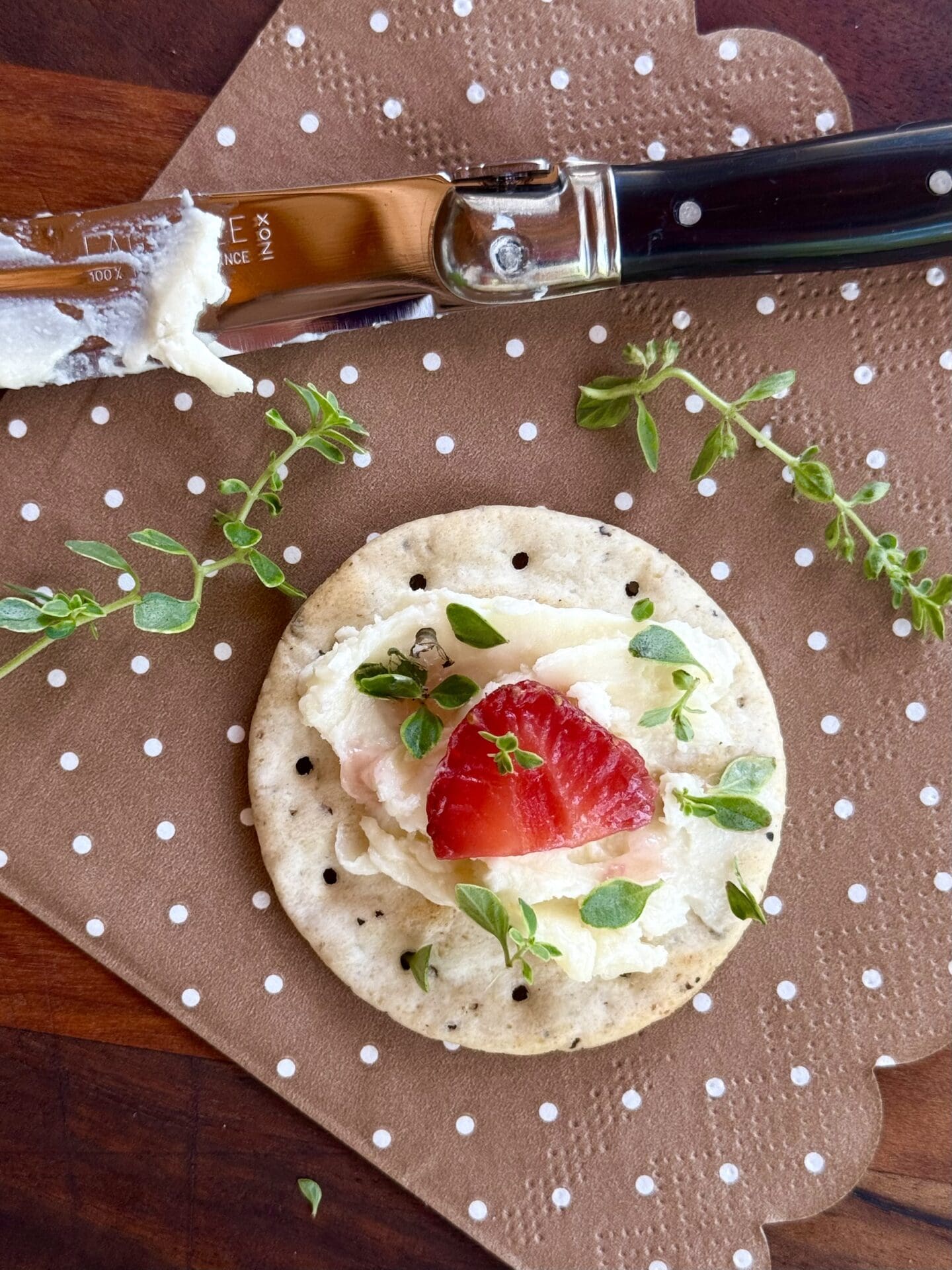 A cracker is seen from above, loaded with a generous swirl of whipped Brie and topped with strawberry and fresh thyme.